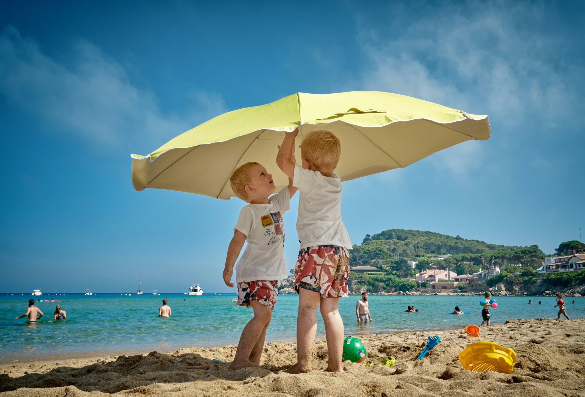 Zwei Kinder spielen unter einem Sonnenschirm am Strand