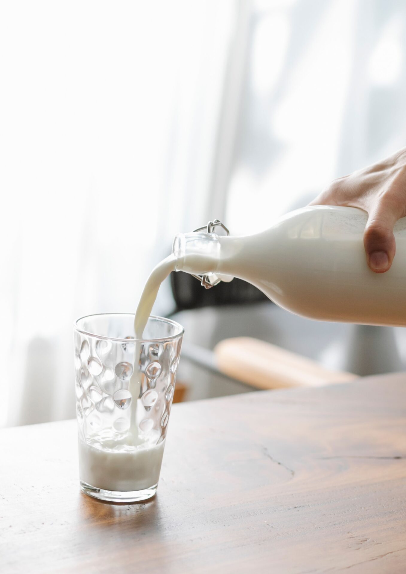 Weisses Milchgetränk wird aus einer Glasflasche in ein Glas eingeschenkt