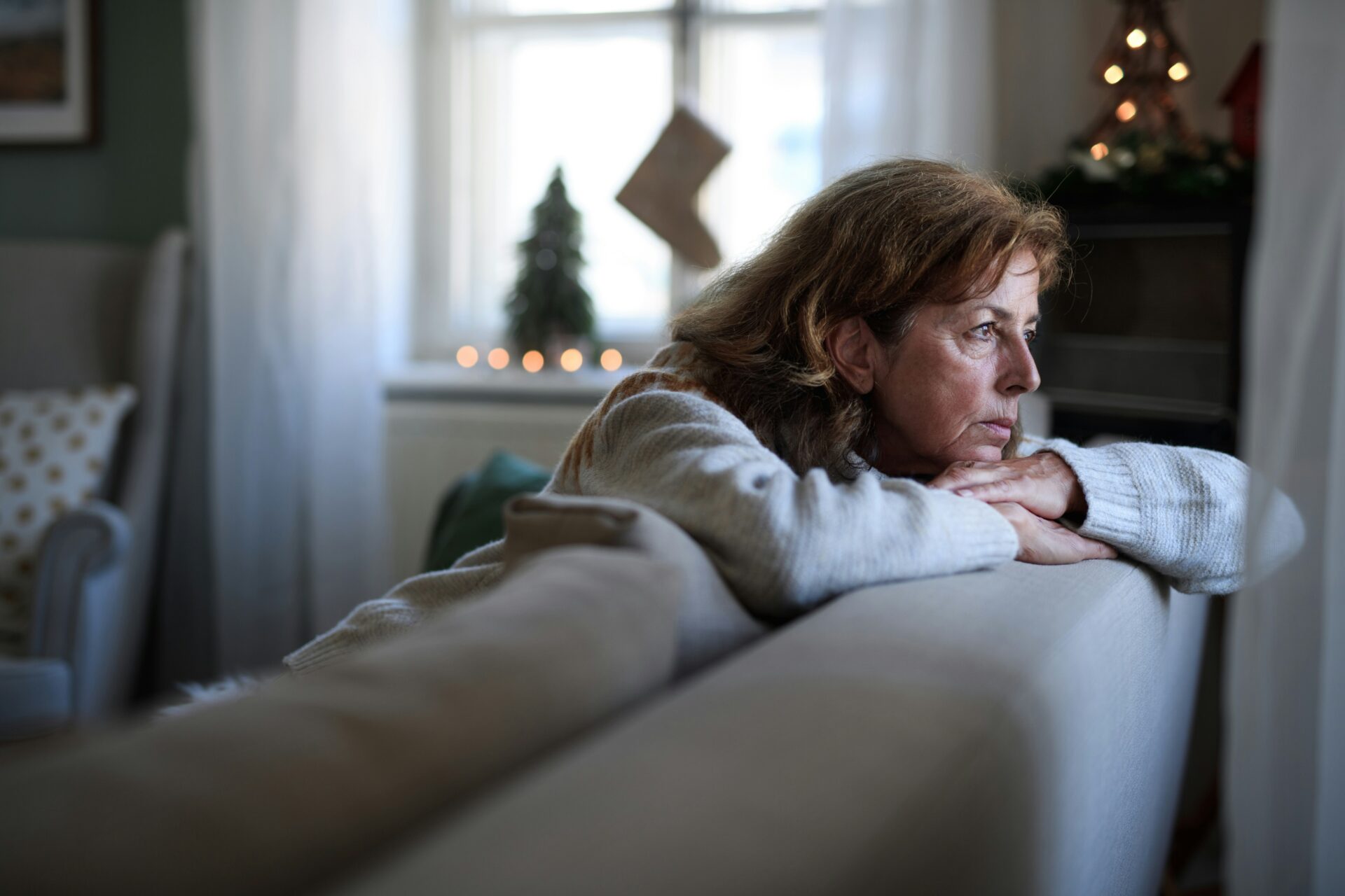 Frau mittleren Alters sitzt nachdenklich auf einem Sofa