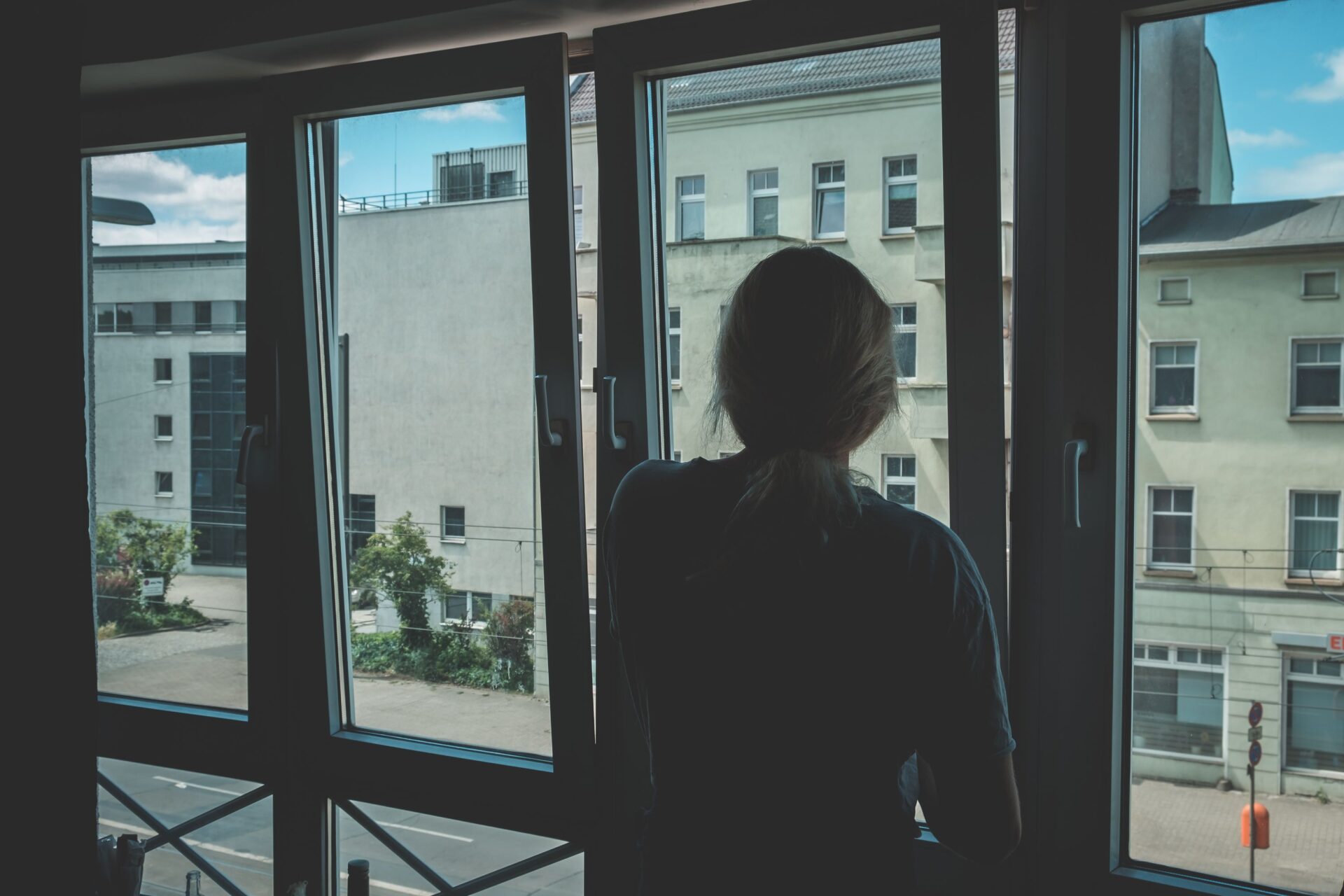 Frau steht mit dem Rücken zur Kamera vor einem geöffneten Fenster