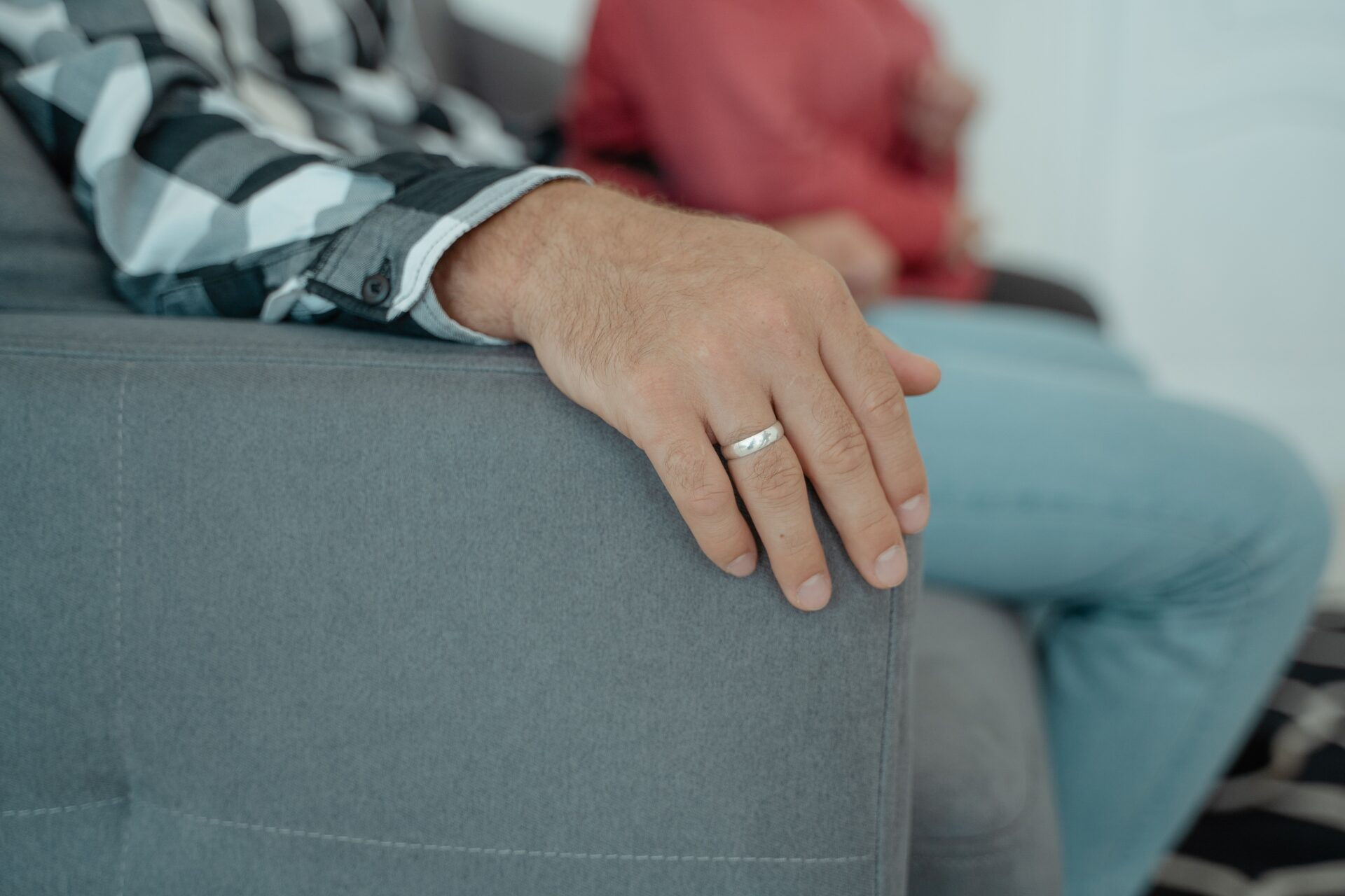 Hand einer sitzenden Person mit Ring auf der Lehne eines grauen Sofas