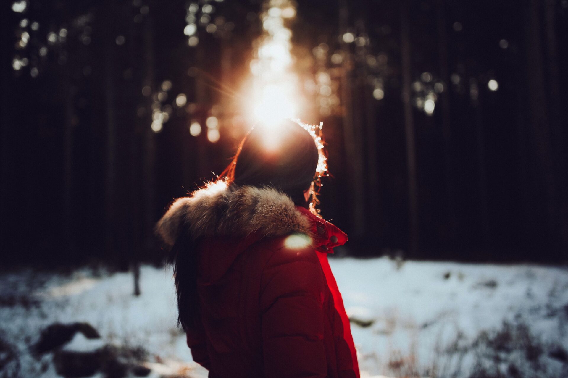 Person in warmer Winterkleidung steht bei Sonnenschein im Schnee