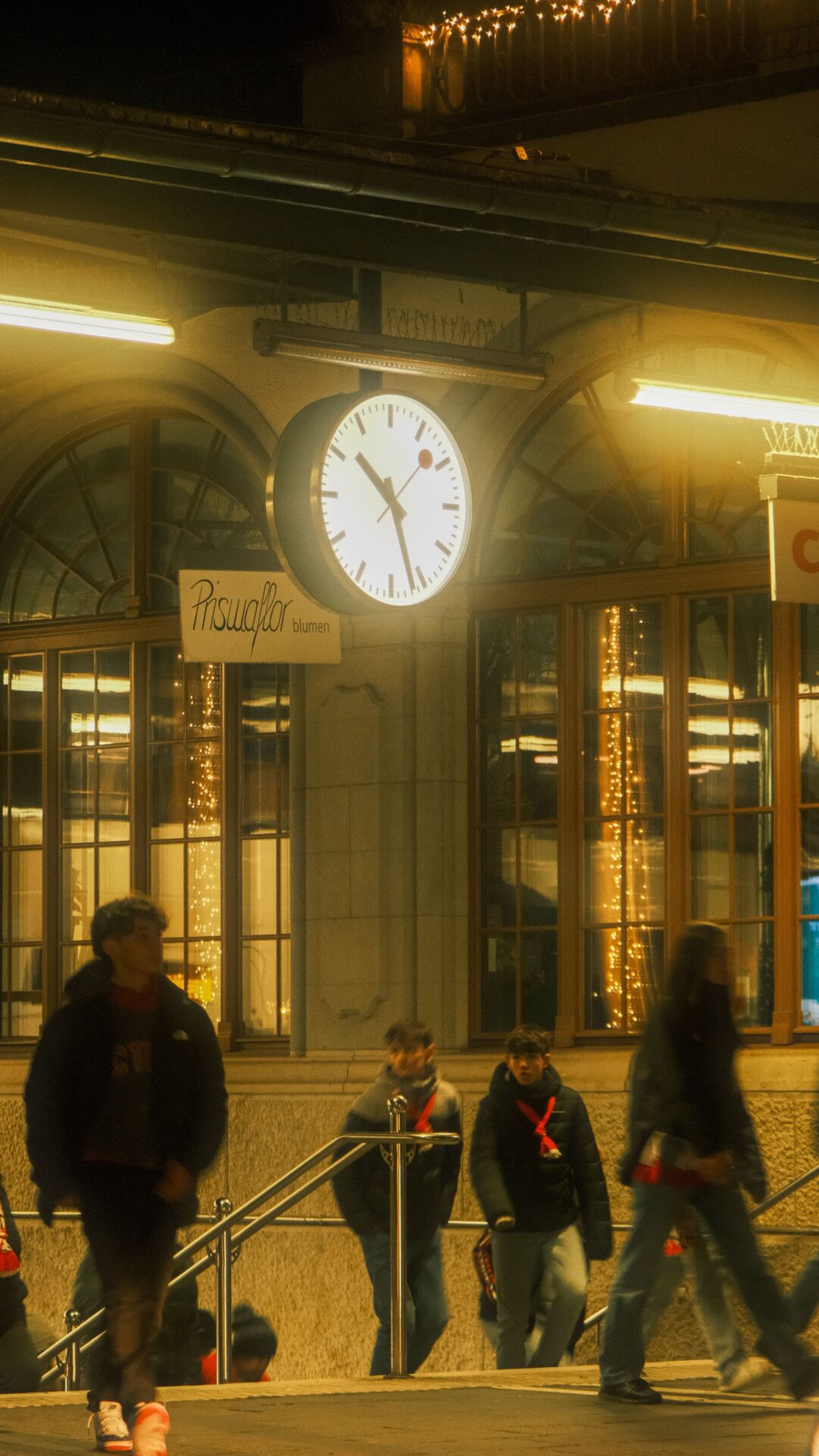 Beleuchtete Bahnhofsuhr mit vorbeigehenden Menschen